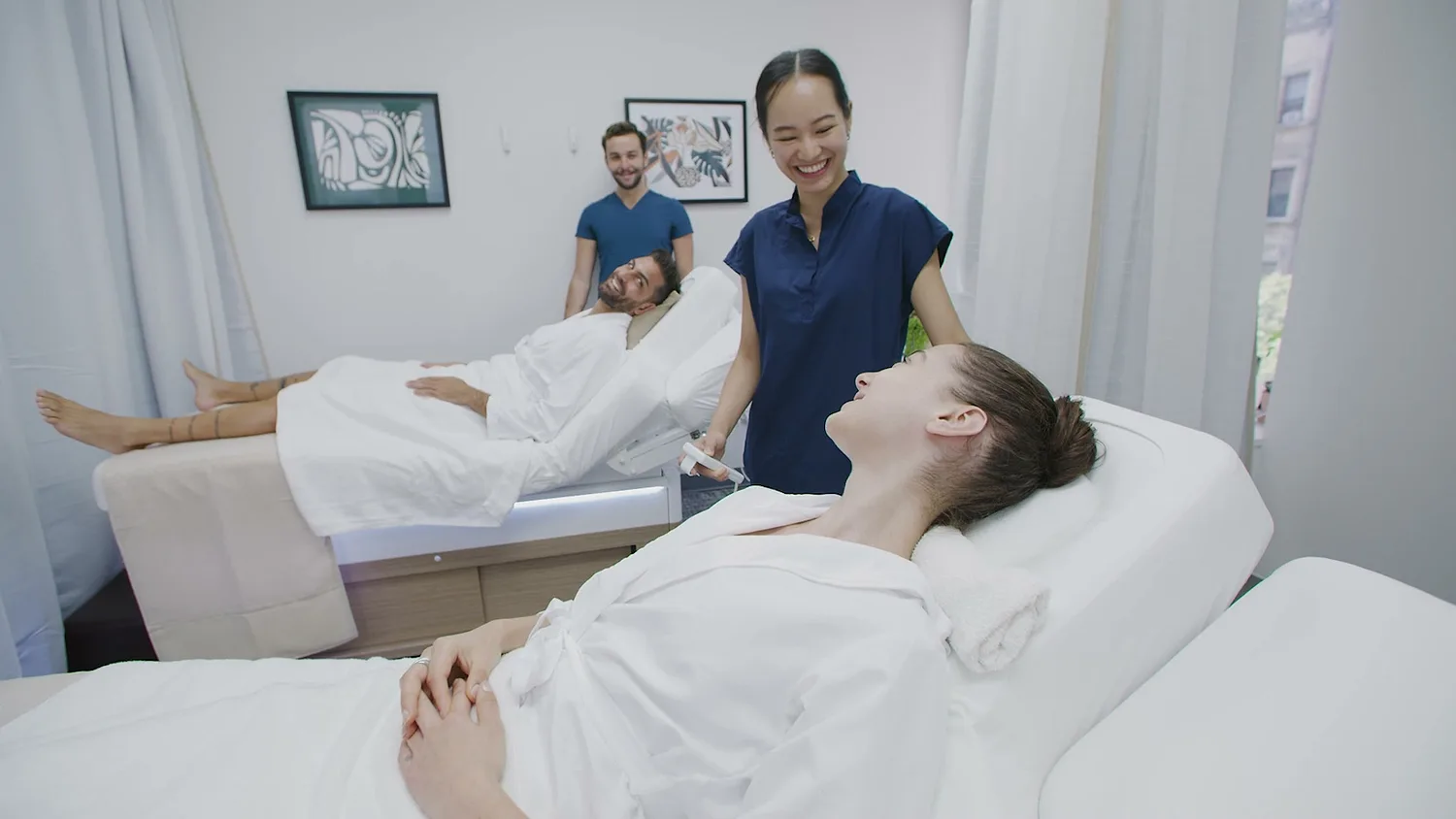 A smiling couple side by side on treatment beds with their therapist
